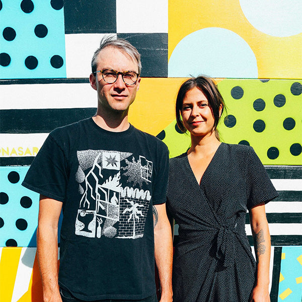 Mikhail Miller and Rachel Ziriada (AKA Nasarimba) standing in front of a bold mural.