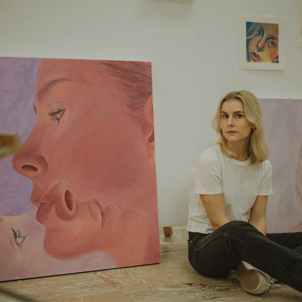 Rowen Dinsmore sitting on the floor in her studio next to a self-portrait.