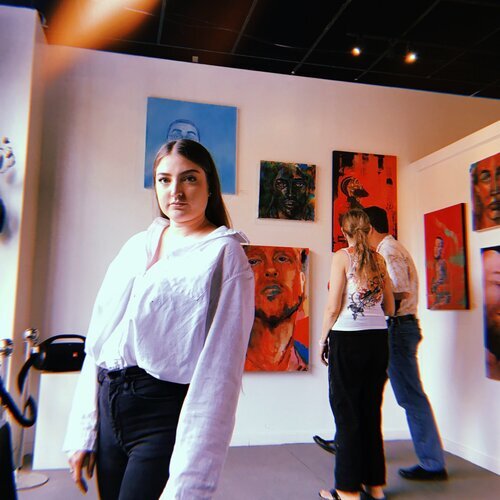 Emily Zdunich standing in an art gallery filled with her paintings.