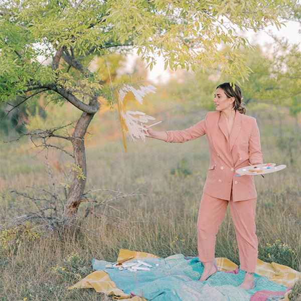 Fawn De Nysschen in a field under a tree painting on a sheet of clear plastic.