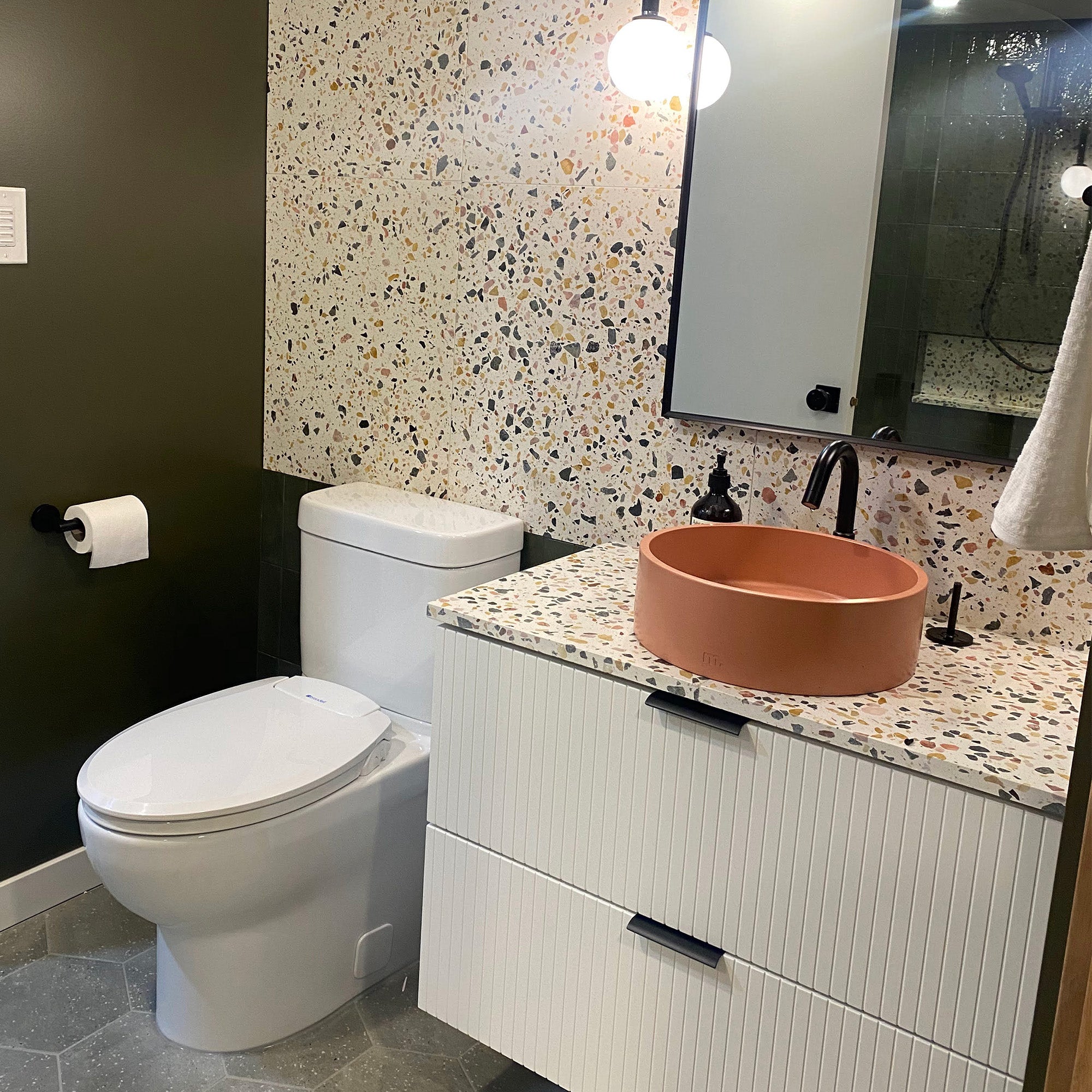 Modern bathroom with a round terra cotta colored sink and cream counters with black and orange specks.